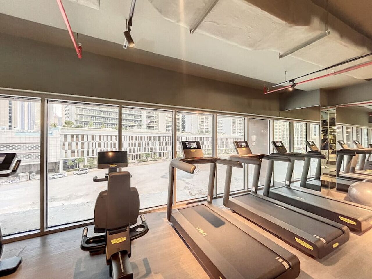 A gym with treadmills, a stationary bike, and a rowing machine. Large windows offer a view of the city.