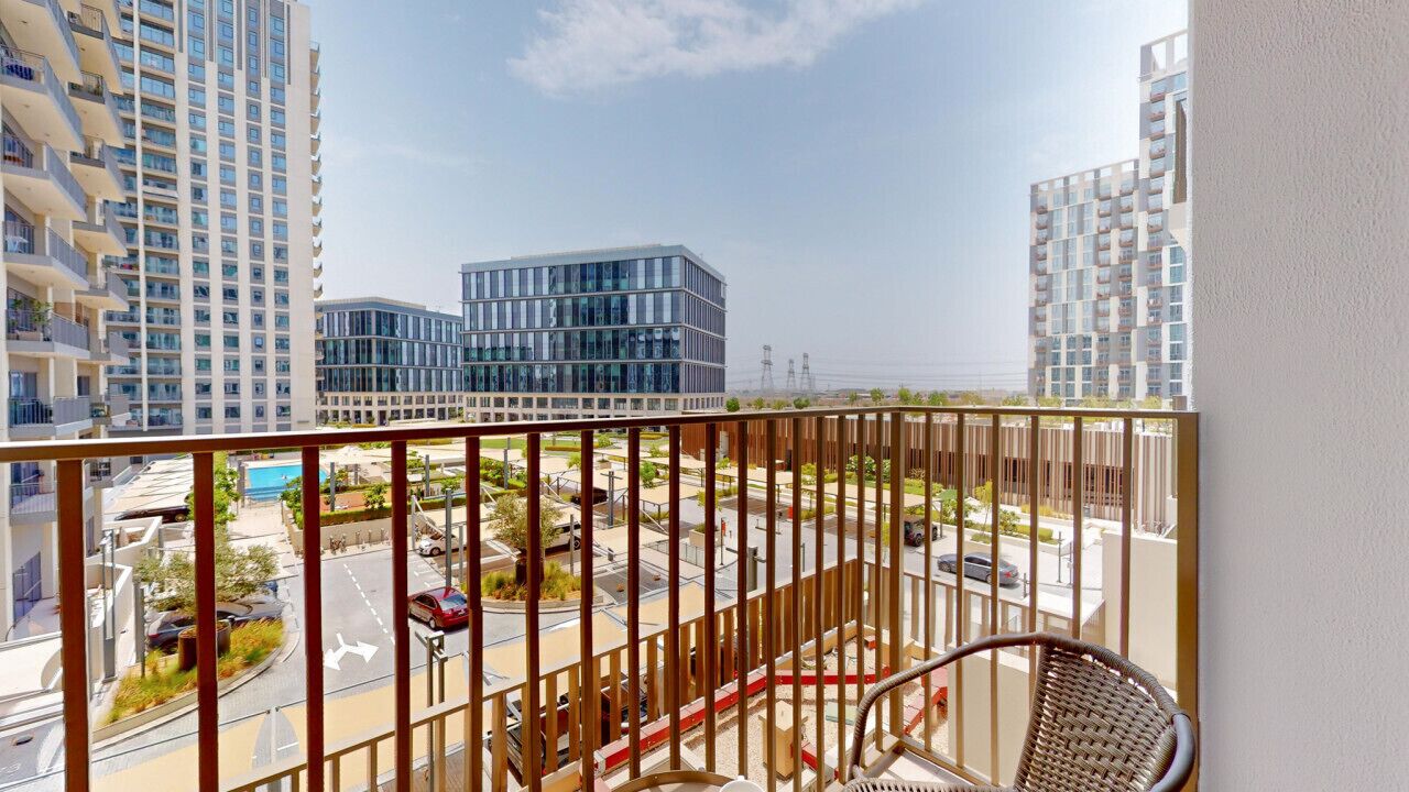Un balcon offrant une vue sur des immeubles modernes, une route et un ciel dégagé.