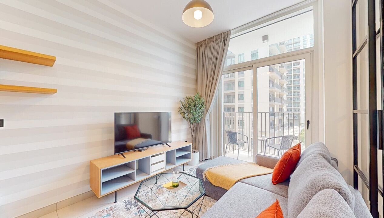 A modern living room with a flat-screen TV, a sofa, a coffee table, and a large window offering a view of the city.