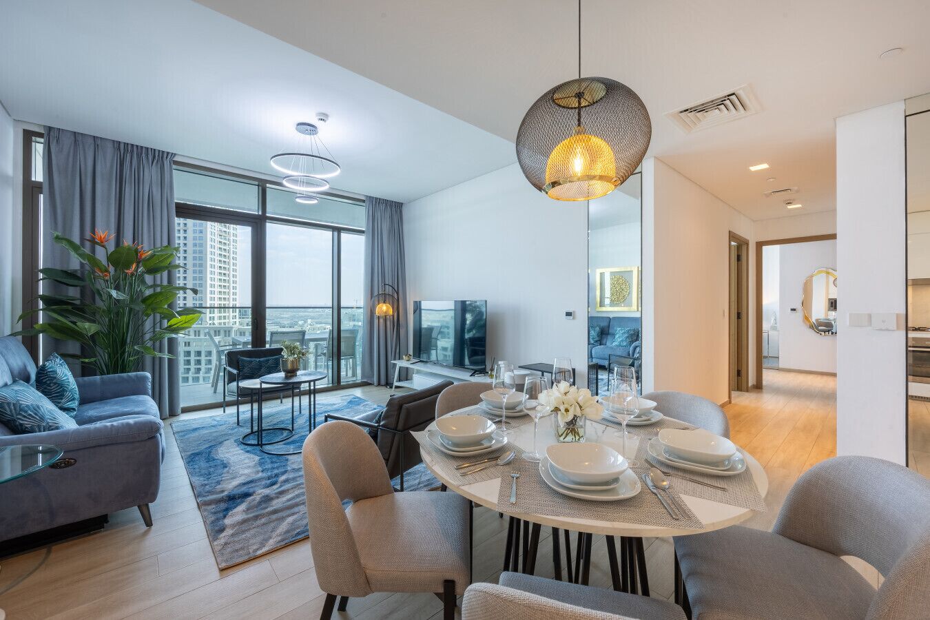 A modern dining area with a round table set for four, a sofa, and a large window offering a city view.