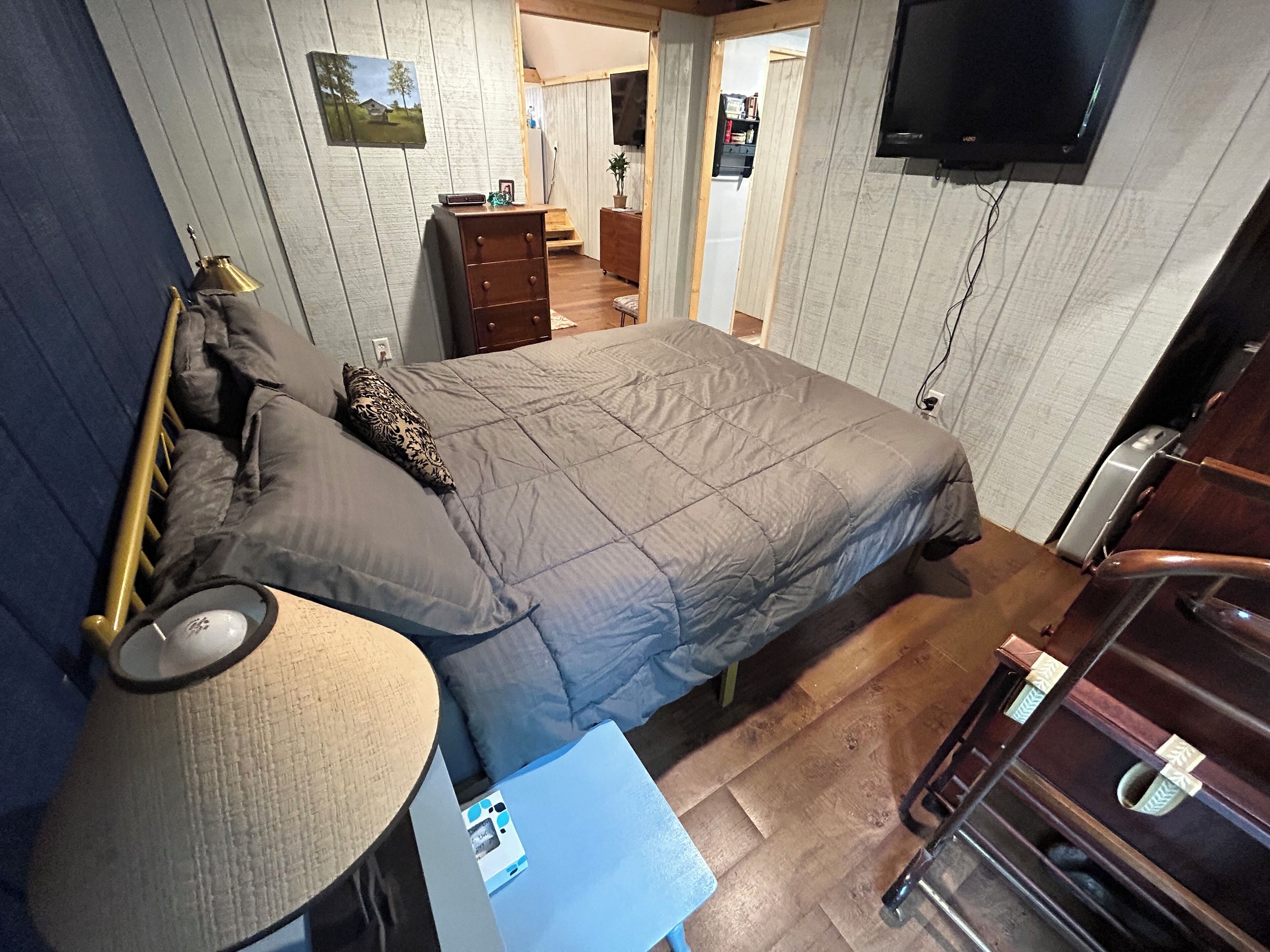 A bedroom with a bed, bedside table, lamp, dresser, and a TV mounted on the wall.