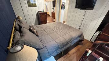 A bedroom with a bed, bedside table, lamp, dresser, and a TV mounted on the wall.