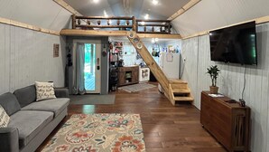 Un vaste salon doté d’un escalier en bois menant à l’étage supérieur, d’un canapé, d’une table basse et d’un téléviseur fixé au mur.