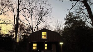 Une petite cabane à un seul étage, dotée d’un porche et de deux fenêtres, entourée d’arbres.