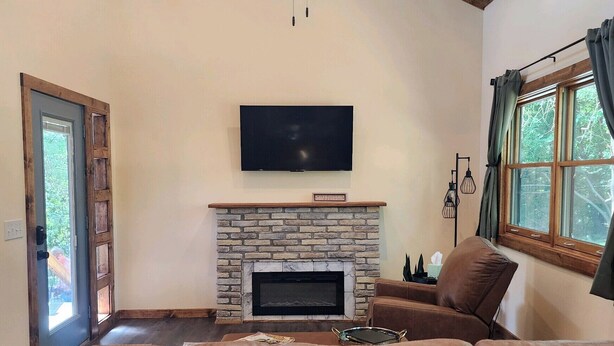 Una sala de estar con un sofá de cuero marrón, chimenea, ventilador de techo y televisor montado en la pared.