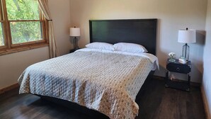 Una cama bien tendida con una colcha acolchada, un cabecero de madera y una mesita de noche con una lámpara y un pequeño jarrón con flores.