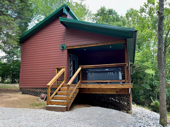 A small, single-story cabin with a wooden deck and a staircase leading to a covered porch.