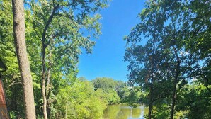 Una terraza de madera que da a un lago, rodeado de árboles y un sendero de grava.