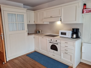 A compact kitchen with white cabinetry, a microwave, a coffee maker, and a stove.