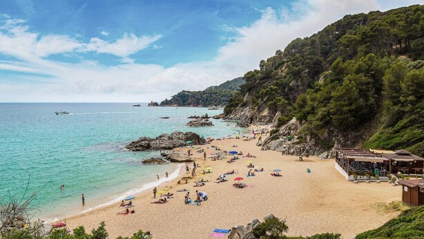 Una playa con aguas turquesas cristalinas, afloramientos rocosos y un promontorio cubierto de bosque.