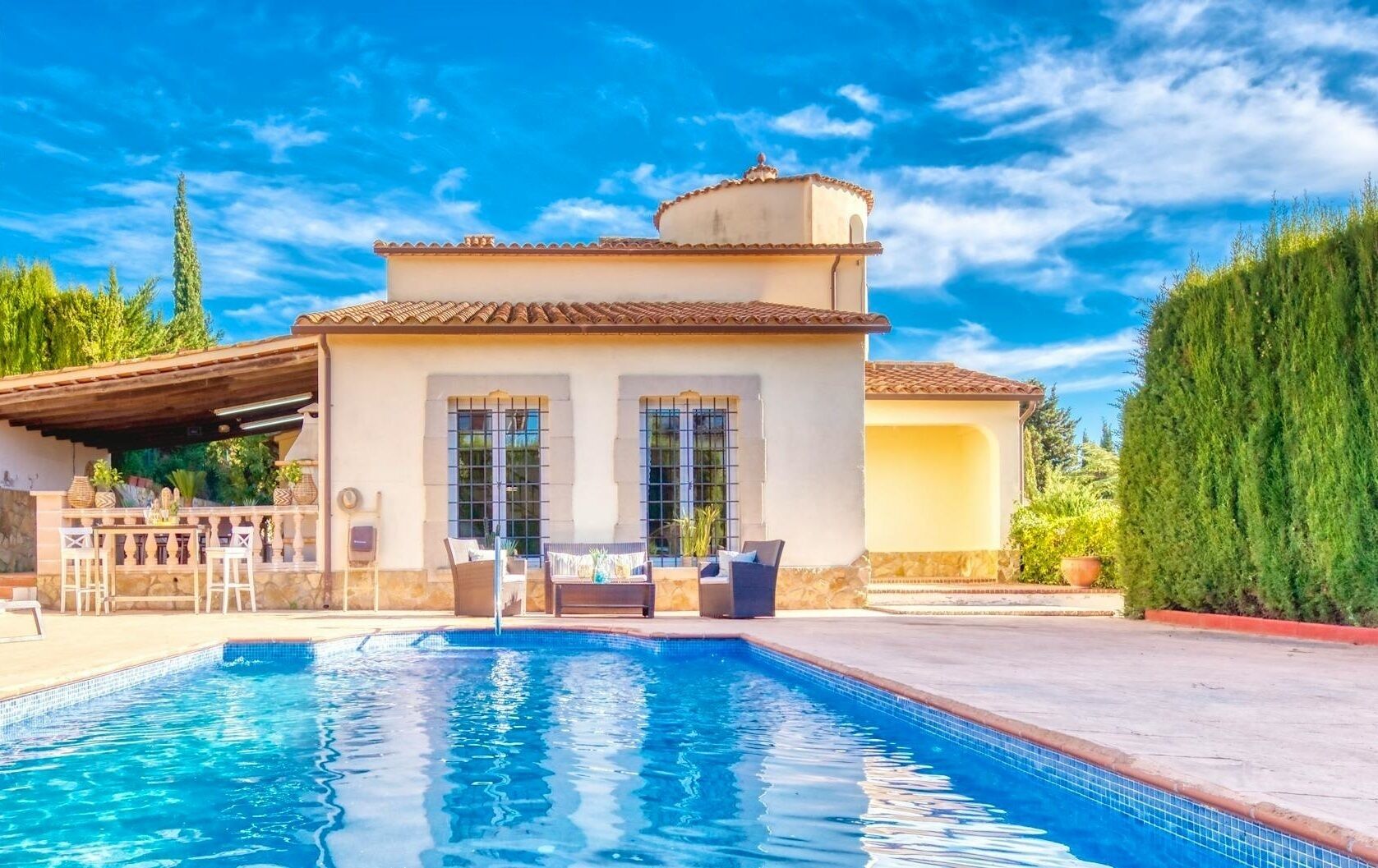 Una zona junto a la piscina con piscina, mobiliario de exterior y un edificio con tejado de azulejos.