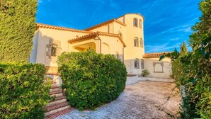 Un edificio de estilo mediterráneo con un patio, escalones que conducen a la entrada y abundante vegetación circundante.
