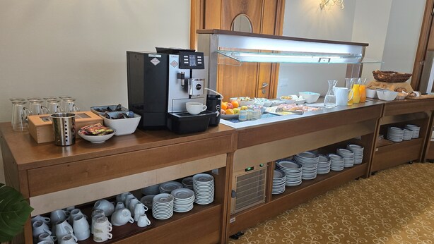 Een buffetopstelling met een koffieapparaat, kommen vol fruit en diverse ontbijtartikelen.