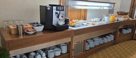 A buffet setup with a coffee machine, bowls of fruits, and a variety of breakfast items.