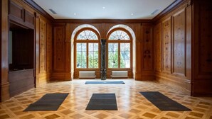 A spacious room with wooden paneling, large arched windows, and a parquet floor.