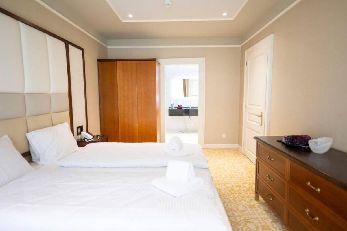 Ein Hotelzimmer mit zwei Betten, einem Holzschrank, einem Nachttisch mit Lampe und einem durchgehenden Türrahmen sichtbaren Badezimmer.