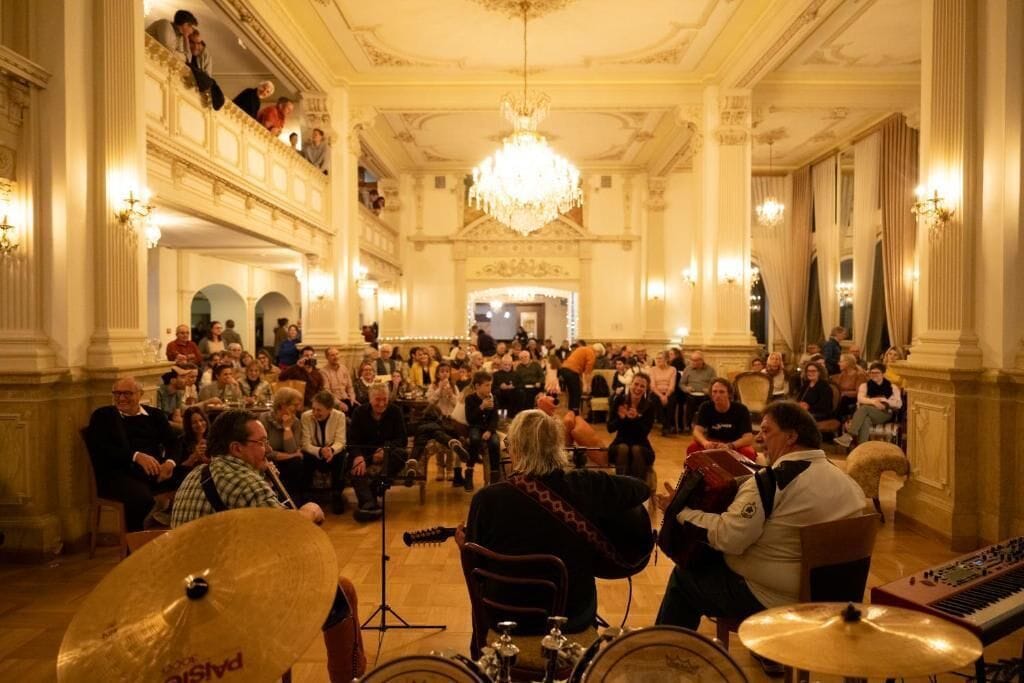 Un salón imponente con columnas ornamentadas, un candelabro y una multitud de personas.