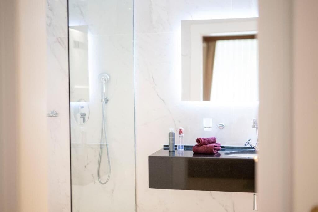 A modern bathroom with a glass-enclosed shower, a dark countertop sink, and a mirror above it.