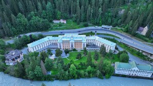 A large, multi-story building with a central courtyard, surrounded by dense forest and a river.