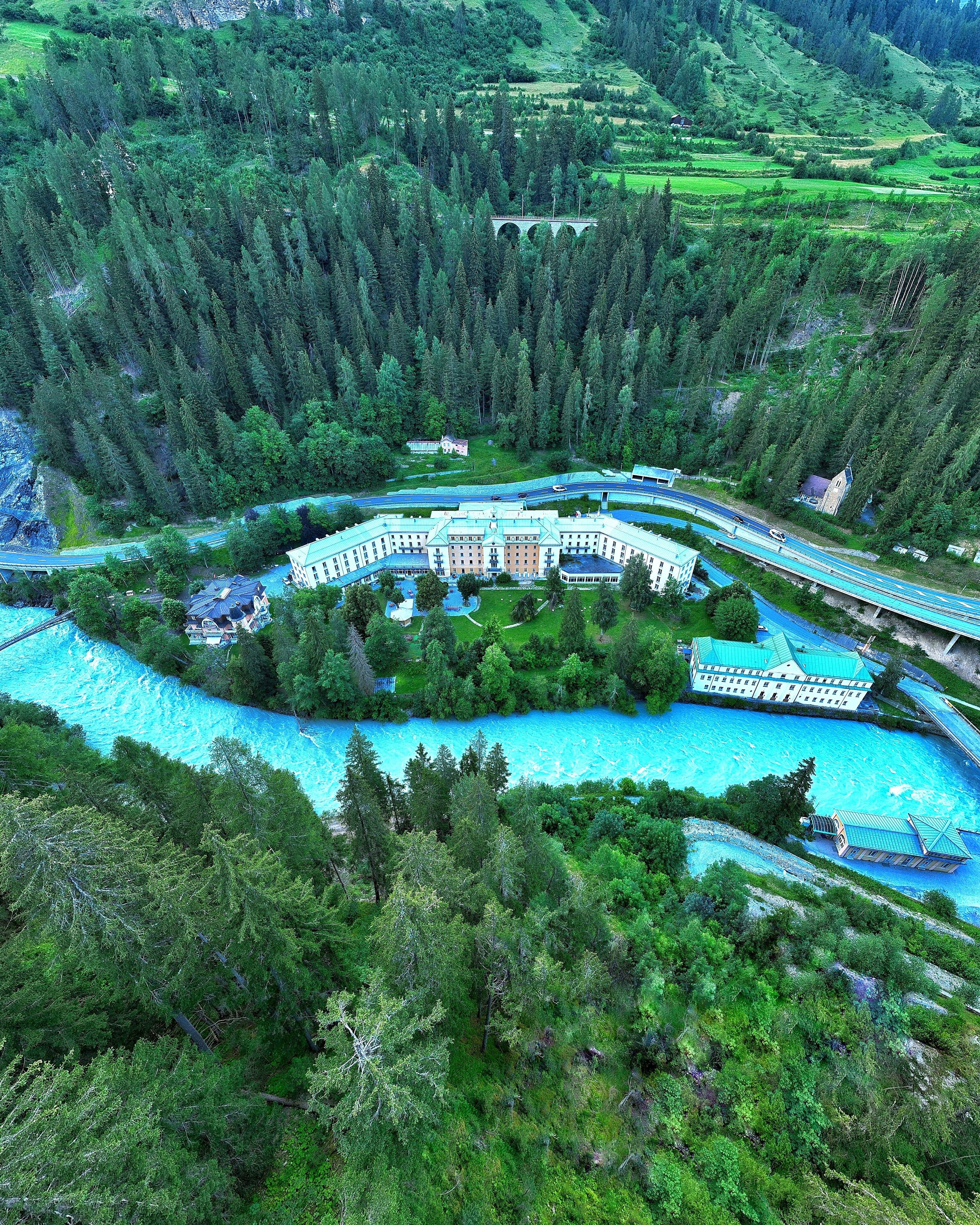 A resort with a central building surrounded by a lake, connected by bridges, and surrounded by dense forest.