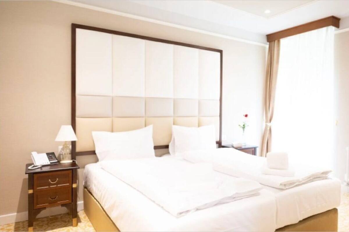 Ein Hotelzimmer mit einem großen Bett, einem Nachttisch mit Lampe und einem Fenster mit Vorhängen.
