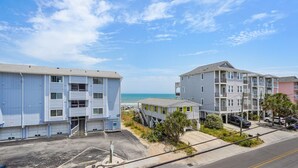 A beachfront residential area with multi-story buildings, including a blue building with a visible garage and a staircase leading to the beach. - Sea Lion`s Den - Ocean View Condo, Steps to Sand (Carolina Beach)