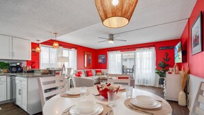 A modern kitchen with white cabinets, a dining area with a round table set for two, and a living room with a sofa and a coffee table. - Sea Lion`s Den - Ocean View Condo, Steps to Sand (Carolina Beach)
