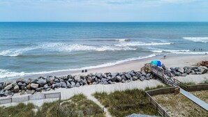 A beach with a wooden walkway, a rocky barrier, and a clear view of the ocean. - Sea Lion`s Den - Ocean View Condo, Steps to Sand (Carolina Beach)