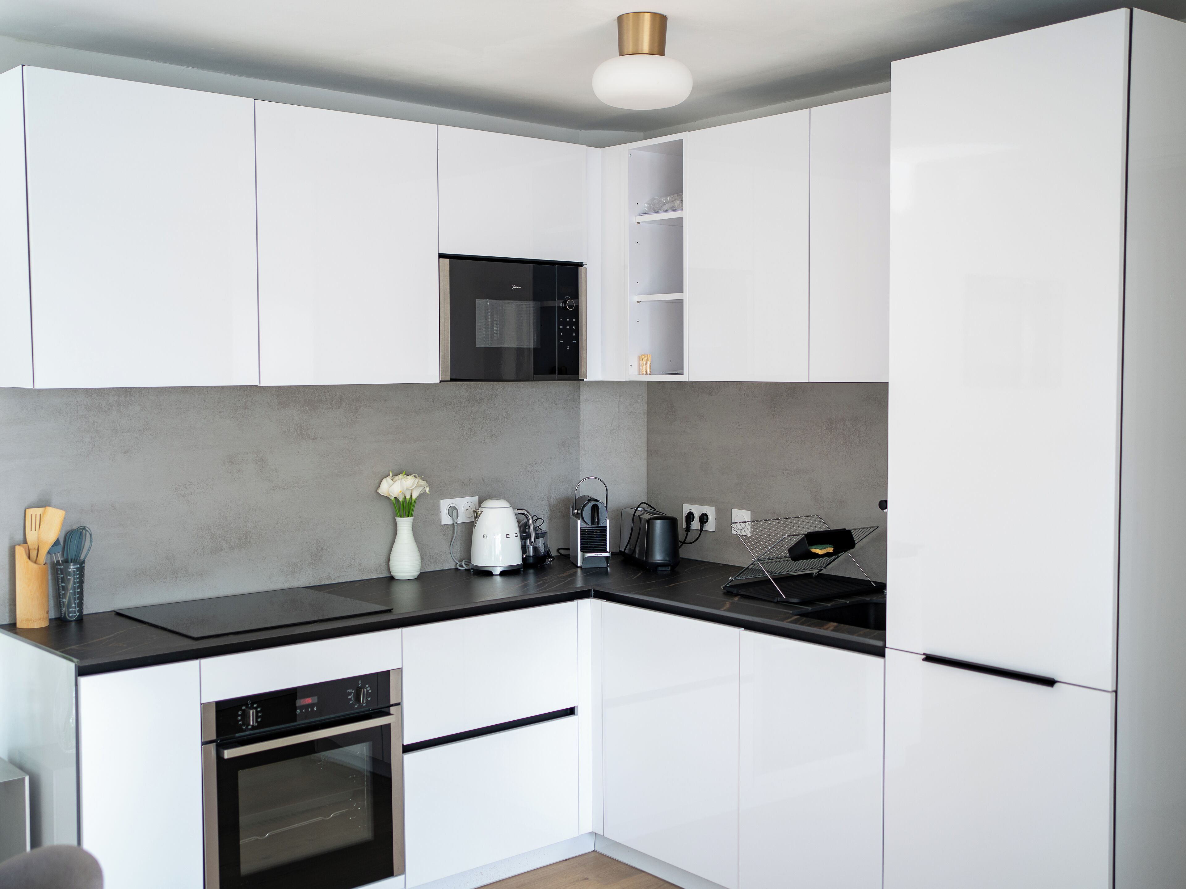 Eine moderne Küche mit weißen Schränken, einer schwarzen Arbeitsplatte, einer eingebauten Mikrowelle, einem Backofen und einer Kaffeemaschine.