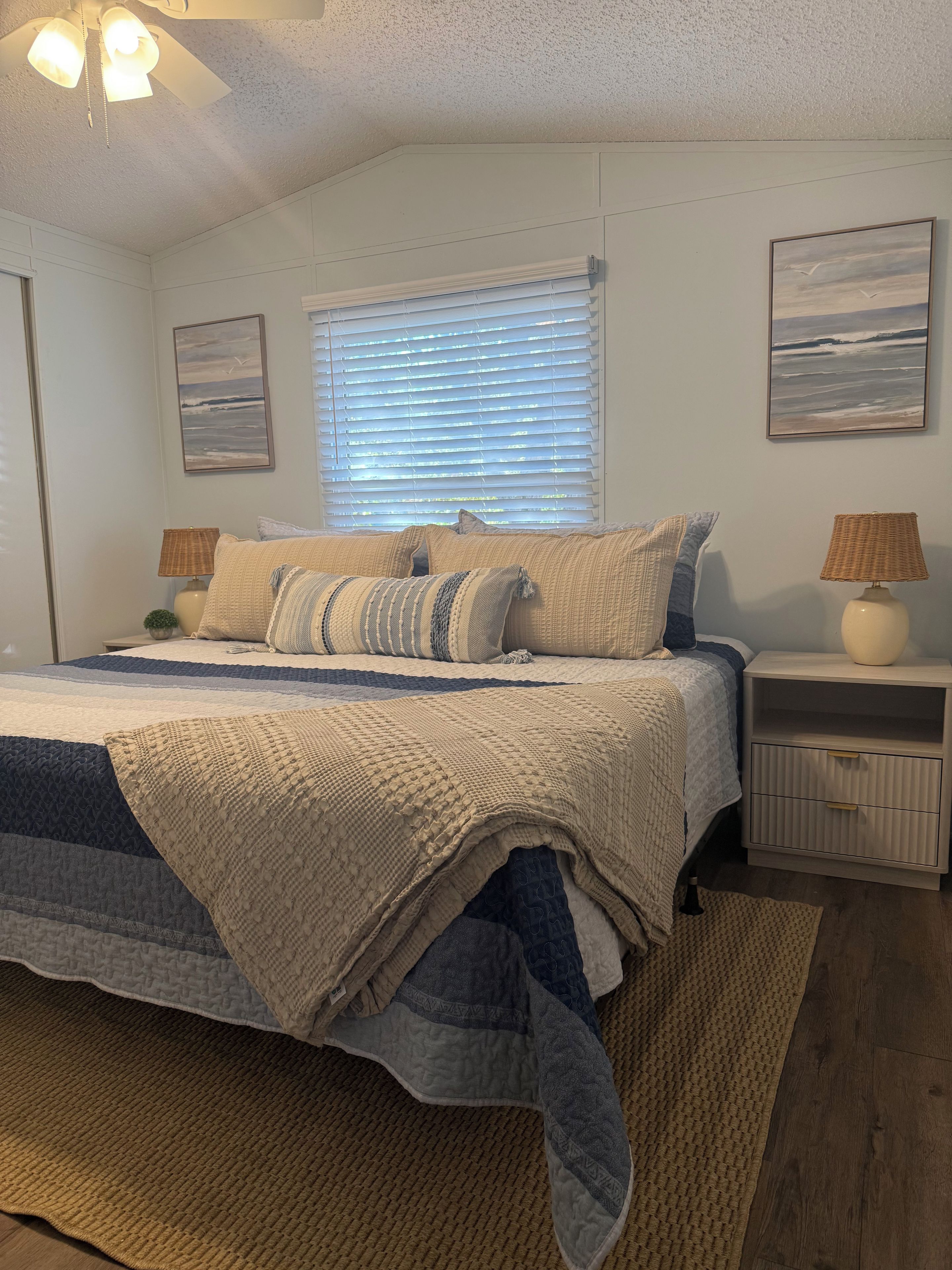 A bedroom with a bed, two nightstands, a window with blinds, and two wall-mounted lamps.