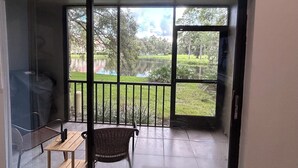 A balcony with a view of a lake and trees, a wicker chair, and a small table with a bottle.