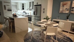 A modern kitchen with white cabinets, a central island, and a dining area with white chairs.