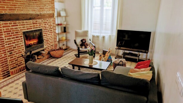 A cozy living room with a brick fireplace, a sofa, a television, and a window with curtains.