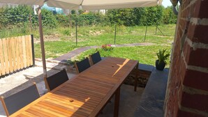 A wooden table and chairs under an umbrella, with a brick wall and a garden in the background.