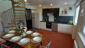 A modern kitchen with a dining area, featuring a staircase, built-in appliances, and a window with curtains.