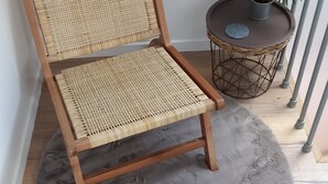 A wicker chair with a wooden frame and a grey shaggy rug on a wooden floor.