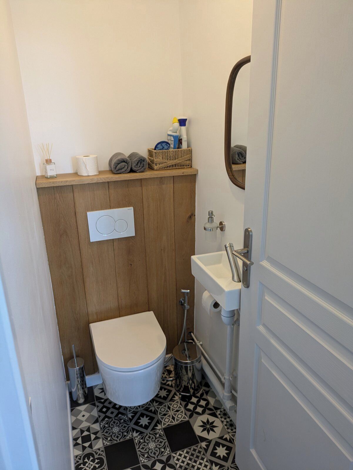 Et lille badeværelse med toilet, vask og en hylde med toiletartikler.