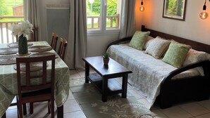 Un salon confortable avec un canapé, une table à manger, des chaises et une vue sur la verdure à l’extérieur.