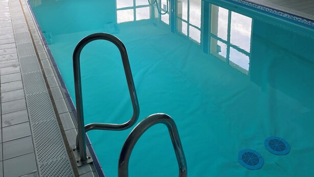 Une piscine intérieure à l’eau d’un bleu cristallin, avec un escalier et plusieurs chaises longues.