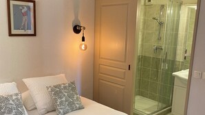 Une chambre à coucher comprenant un lit, des oreillers, une lampe fixée au mur, une porte et un espace douche.