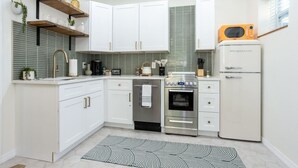A compact kitchen with white cabinets, a stainless steel oven, a microwave, and a refrigerator. - Mockingbird Bungalow min to beaches (Gulfport)