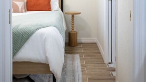 A bedroom with a bed, a bedside table, a wall-mounted air conditioner, and a framed picture on the wall. - Mockingbird Bungalow min to beaches (Gulfport)