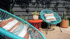 A patio with two turquoise wicker chairs, a red table, and a striped cushion. - Mockingbird Bungalow min to beaches (Gulfport)