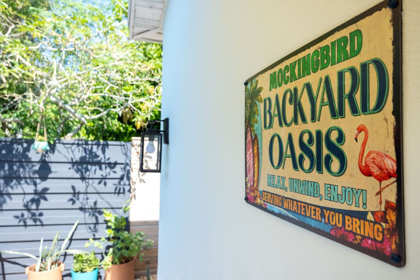 Une enseigne pour « Mockingbird Backyard Oasis », avec une illustration de flamant rose et un texte invitant les visiteurs à se détendre et à profiter de l’endroit.