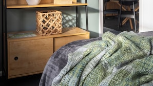 Ein Zimmer mit einem Bett, einem Holzboden mit Dekorationen, einer Zimmerpflanze und einer Tür zu einem Essbereich.