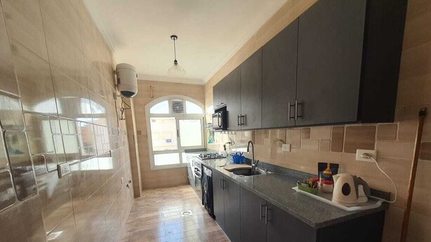 A modern kitchen with dark cabinets, a granite countertop, and a built-in microwave. - 2-bedroom apartment in terrific New Cairo with WiFi (Industrial Area)