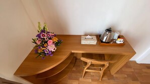 Un escritorio de madera con un taburete pequeño de madera, un ramo de flores, una caja de pañuelos, un hervidor y una taza.