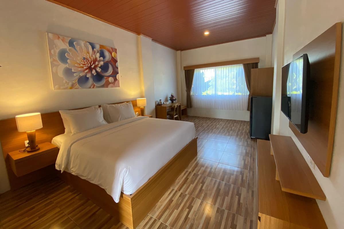 A hotel room with a large bed, a flat-screen TV, a painting, and a window with curtains.