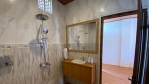 Un baño con piso de madera, pared de mármol, lavamanos con espejo y ducha con cabezal de ducha manual.