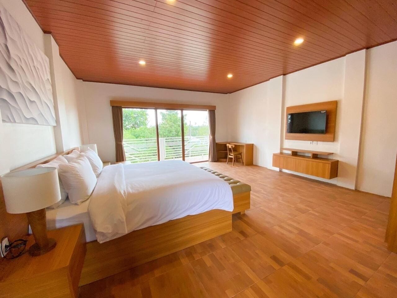 A bedroom with a large bed, a television mounted on the wall, and a wooden floor.